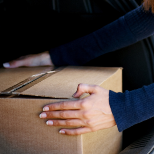 A cardboard box being put in the trunk of a car.